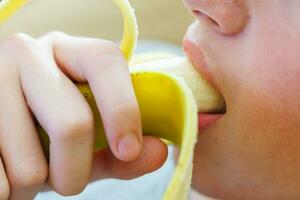 portrait de une adolescent garçon en mangeant une banane. photo de une gars bouche et lèvres avec une banane. Frais fruit. en bonne santé nourriture pour les enfants