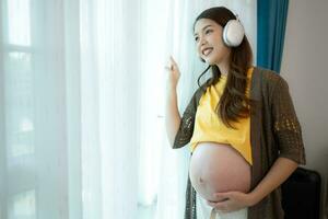 avec écouteurs sur sa estomac, une Enceinte mère laisser sa bébé à Ecoutez à la musique dans le utérus. photo