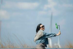 Jeune magnifique brunette femme avec longue cheveux portant une bleu veste, noir des lunettes de soleil, et en portant une miniature Moulin à vent photo