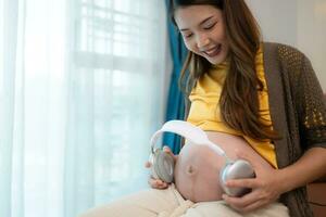 avec écouteurs sur sa estomac, une Enceinte mère laisser sa bébé à Ecoutez à la musique dans le utérus. photo