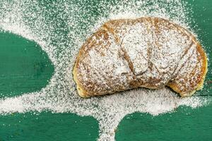 fraîchement cuit des croissants avec en poudre sucre sur une vert rustique table photo