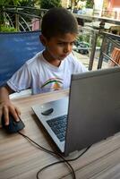 peu garçon séance à table en utilisant portable pour en ligne classe dans classe 1, enfant en train d'étudier sur portable de Accueil pour distance apprentissage en ligne éducation, école garçon les enfants mode de vie concept photo