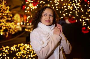 souriant content femme en marchant dans Noël marché décoré avec vacances lumières dans le soir. sentiment content dans gros ville. photo