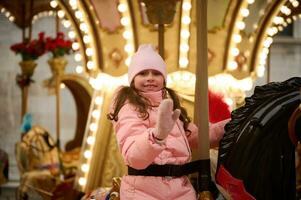 mignonne souriant peu enfant fille équitation une en bois cheval sur joyeux aller rond carrousel à une de fête famille Noël marché photo