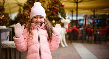 authentique content enfant fille souriant à caméra, profiter le A venir hiver vacances, permanent en plein air à Noël juste photo