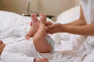 fermer mains de une femme en portant bébé jambes et Faire doux massage mouvements à prophylaxie le plat pieds photo