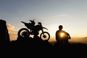homme avec motocross bicyclette contre magnifique lumières, silhouette de une homme avec motocross moto sur Haut de Roche haute Montagne à magnifique coucher de soleil, enduro moto Voyage concept. photo