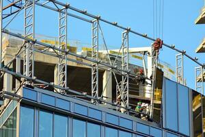 haute monter bâtiment en dessous de construction. installation de verre façade panneaux sur une renforcé béton structure. photo