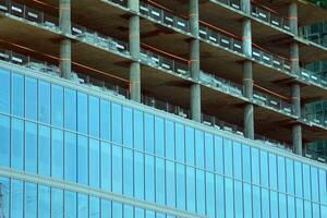 haute monter bâtiment en dessous de construction. installation de verre façade panneaux sur une renforcé béton structure. photo