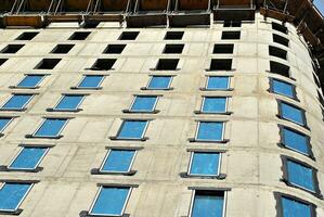 haute monter bâtiment en dessous de construction. installation de verre façade panneaux sur une renforcé béton structure. photo