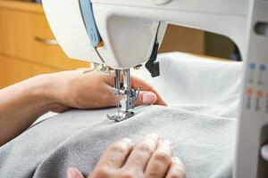 mains féminines cousant du tissu gris sur une machine à coudre moderne. vue rapprochée du processus de couture. photo