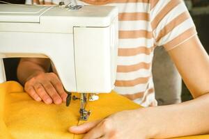 mains féminines cousant du tissu jaune sur une machine à coudre moderne. vue rapprochée du processus de couture. photo
