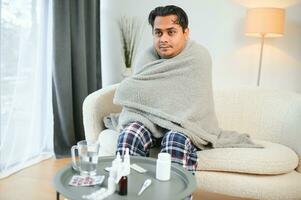 malade Indien homme dans plaid asseoir seul grelottant de froid. mauvais pour la santé arabe gars asseoir sur chaise sentiment malaise essayer à chauffage en haut photo
