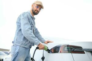 homme en portant Puissance mise en charge câble pour électrique voiture dans Extérieur voiture parc. et il s Aller à relier le voiture à le mise en charge station dans le parking lot près le achats centre. photo