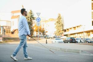 Jeune aveugle homme avec blanc canne en marchant à travers le rue dans ville photo