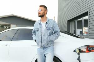 magnifique Jeune élégant homme est avec électrique voiture à jour mise en charge le véhicule photo