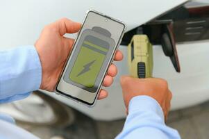 décontractée homme avec téléphone intelligent près électrique voiture attendre pour le terminer de le batterie mise en charge processus photo