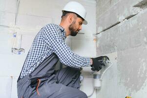 horizontal instantané de Jeune plombier travail avec gris égout tuyaux, fixation leur à mur avec une Aidez-moi de Tournevis. photo