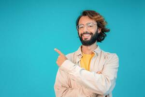 souriant adulte homme présenter produit, montrer du doigt doigt contre bleu Contexte avec copie espace. photo
