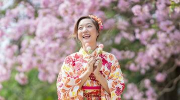 Japonais femme dans traditionnel kimono robe en portant sucré hanami dango dessert tandis que en marchant dans le parc à Cerise fleur arbre pendant printemps Sakura Festival photo