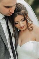 portrait de le la mariée et jeune marié dans la nature. le jeune marié et le brunette la mariée dans une blanc longue robe sont étreindre et à la recherche bas. élégant jeune marié. magnifique cheveux et maquillage photo