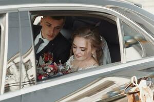 une moderne la mariée et jeune marié dans une dentelle robe dans une voiture la fenêtre. magnifique et souriant jeunes mariés. content vacances. photo