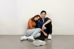 portrait de de bonne humeur et souriant Jeune asiatique couple dans décontractée tenues séance sur sol et à la recherche à caméra. photo