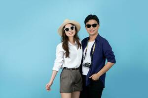 espiègle et content asiatique touristique couple portant été vêtements à aller sur vacances. elles ou ils supporter seul sur une bleu Contexte. photo