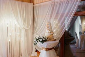 une blanc mariage gâteau, décoré avec fleurs et or, des stands sur une verre rester. Frais fleurs à le mariage. bonbons photo