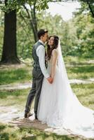 élégant Jeune mariées, content sur leur jour, prendre plaisir chaque autre. en portant mains dans une printemps parc. portrait. printemps mariage. Naturel maquillage photo