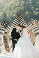 mariage la cérémonie La peinture dans la nature. le la mariée et jeune marié supporter près le d'or cambre pendant le La peinture la cérémonie et baiser, couvert avec une bouquet. un cambre dans le forme de une tulipe et Frais fleurs photo