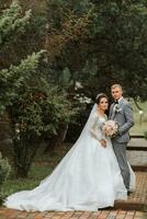 Beau jeune marié et charmant la mariée ensemble dans le parc. portrait. luxueux robe avec une longue train. élégant Jeune jeune marié. mariage bouquet. luxe mariage photo