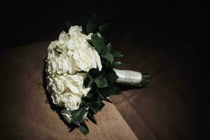 une bouquet de blanc des roses et verdure sur une marron Contexte. une magnifique photo avec détails de le mariage. mariage journée. contour lumière. ombres et lumière