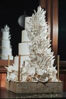 blanc Royal mariage gâteau décoré avec fleurs et décoratif plumes fabriqué de Chocolat décoré avec or, sur une or rester. Royal mariage, bonbons photo