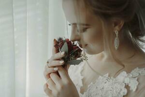 préparation pour le mariage. magnifique Jeune la mariée dans blanc mariage robe à l'intérieur. luxe modèle regards à mariage chaussures, à Accueil dans studio pièce avec gros la fenêtre. le fille spectacles photo