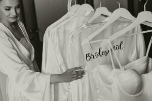 Matin robe de le la mariée et demoiselles d'honneur. Matin préparation de le la mariée. le la mariée dans une blanc mariage robe avec dentelle permanent dans le chambre. sélectif concentrer photo