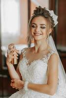 femelle beauté. charmant femme à maison. la mariée vaporisateur parfum élégant femme portant une blanc robe vaporisateur soumissionner parfum. élégant verre bouteille de parfum dans mains. fille avec maquillage et une bouteille de parfum photo