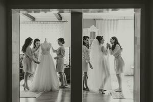 de la mariée petite amie prépare le la mariée pour sa mariage journée. le de la mariée petite amie aide sécurise le de la mariée mariage robe avant le cérémonie. noir et blanc photo