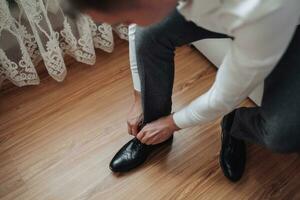 élégant homme porte noir cuir des chaussures sur une en bois Contexte. attacher chaussures. Pour des hommes style. entreprise. Masculin portrait de une Beau gars. le homme est posant photo