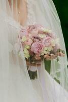 photo de une bouquet de rose pivoines. le la mariée est permanent avec une bouquet dans une blanc robe couvert avec une voile. une magnifique robe. jolie femme. mariage photo