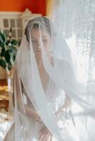 une brunette la mariée dans une blanc robe détient sa mariage bouquet, pose. français manucure. ouvert épaules. magnifique mains. longue voile. Matin de le la mariée. détails photo