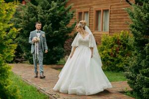 mariage dans la nature. le la mariée des stands dans de face de le jeune marié et regards plus de le sien épaule contre une Contexte de des arbres et une en bois cabane. élégant jeune marié. magnifique la mariée. photo