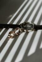 deux or texturé mariage anneaux sur des rayons de chute lumière près une montre-bracelet avec une noir cuir sangle photo