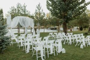 mariage la cérémonie par le lac. une luxueux mariage cérémonie. romantique mariage cérémonie. le présidium est décoré avec blanc fleurs. blanc chaises photo