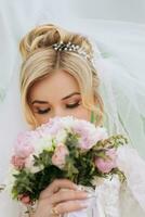 portrait de le la mariée. le la mariée est permanent dans une blanc robe et voile avec une bouquet et reniflement il, dans une vert champ. une magnifique robe. jolie femme. mariage photo