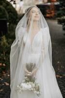 une magnifique la mariée avec sa yeux fermé est permanent en portant sa bouquet. portrait de une Jeune magnifique la mariée. mariage. portrait avec une voile plus de sa visage photo