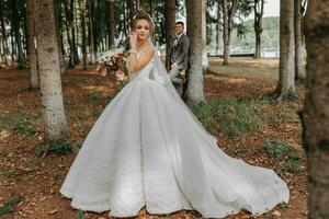 une magnifique Jeune femme dans une mariage robe entre grand des arbres dans le forêt avec une Royal coiffure et une élégant tiare avec une bouquet de fleurs dans sa mains, une mariage dans d'or Couleur photo