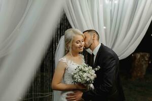 mariage la cérémonie sur le rive de le lac. La peinture la cérémonie dans le soir. romantique peinture. le présidium est décoré avec blanc fleurs. blanc chaises. le la mariée et jeune marié doucement tenir mains photo