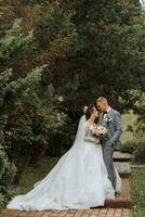 Beau jeune marié et charmant la mariée ensemble dans le parc. portrait. luxueux robe avec une longue train. élégant Jeune jeune marié. mariage bouquet. luxe mariage photo