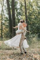 portrait de content la mariée et jeune marié dans le forêt. le jeune marié détient le la mariée dans le sien bras, dansant avec son. photo de le robe dans mouvement. mariage photo session dans la nature.